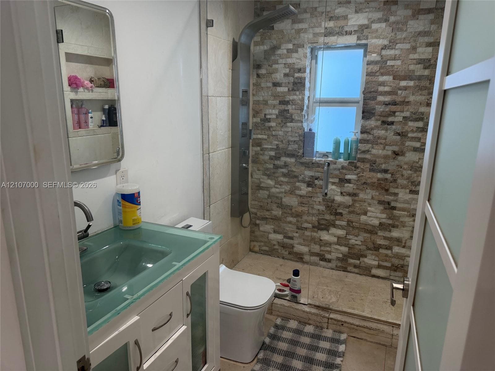Bathroom featuring a vanity with a frosted glass top and integrated sink, a glass-enclosed shower with stacked stone tiling, a multi-jet shower panel system, and built-in wall niches