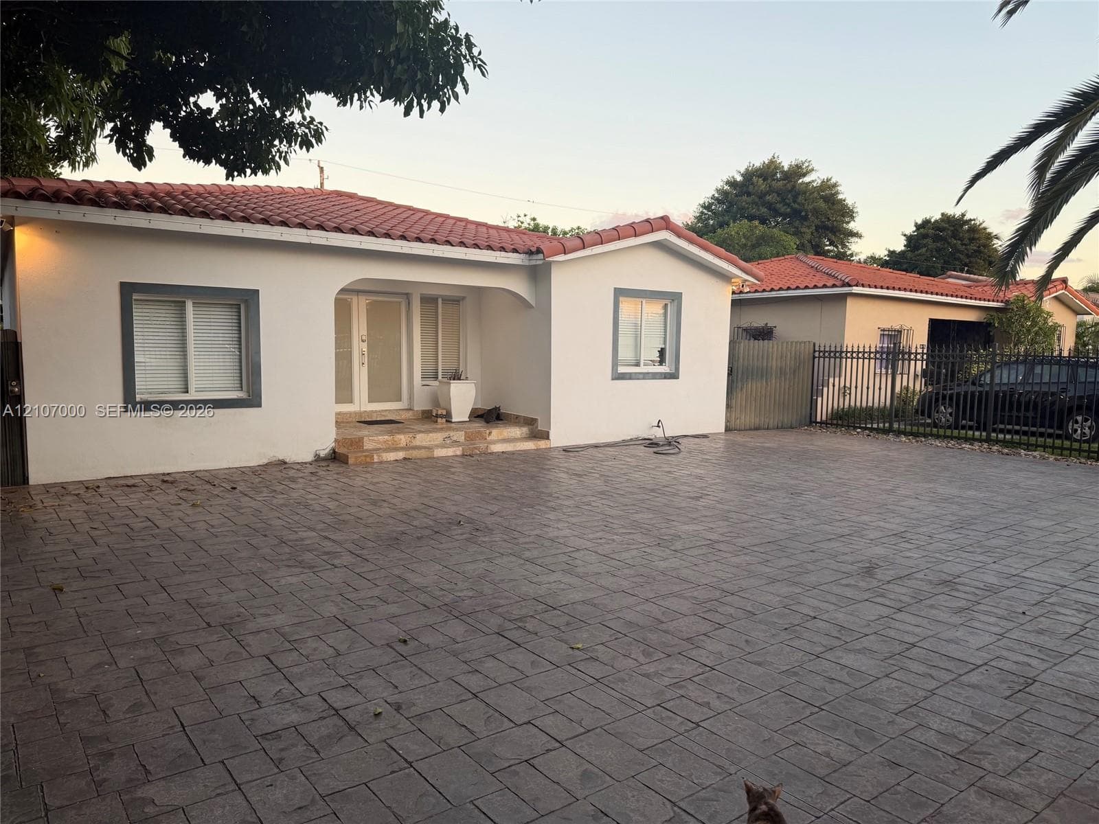 Stucco exterior with a red tile roof featuring an arched entryway, double-door main entrance, and an expansive stamped concrete driveway