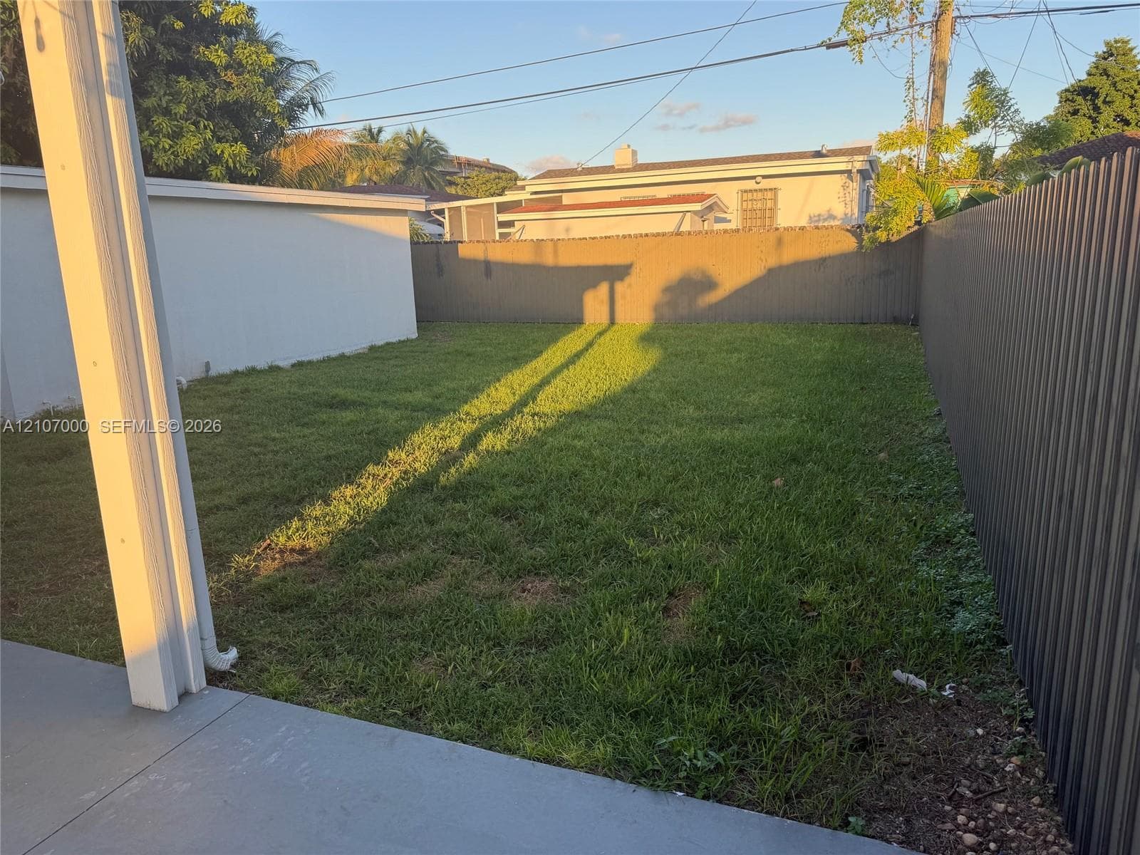 Fenced backyard featuring a concrete patio, grass lawn, and corrugated metal perimeter fencing