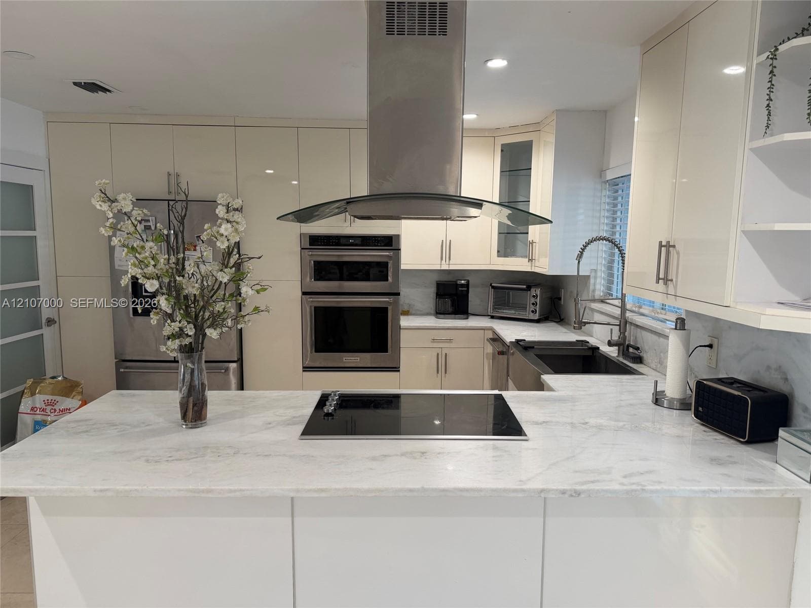 Contemporary kitchen featuring high-gloss cabinetry, stone-surface countertops, a stainless steel wall oven, an integrated cooktop, and a stainless steel range hood