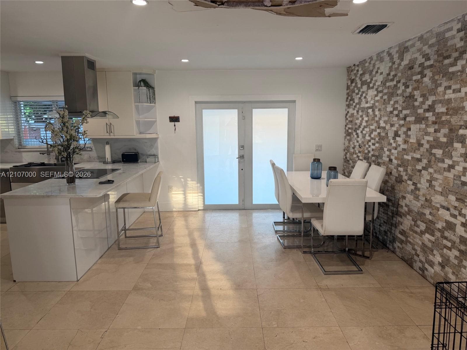 Kitchen featuring a waterfall-edge island, stone-tiled accent wall, recessed lighting, and double-door entry