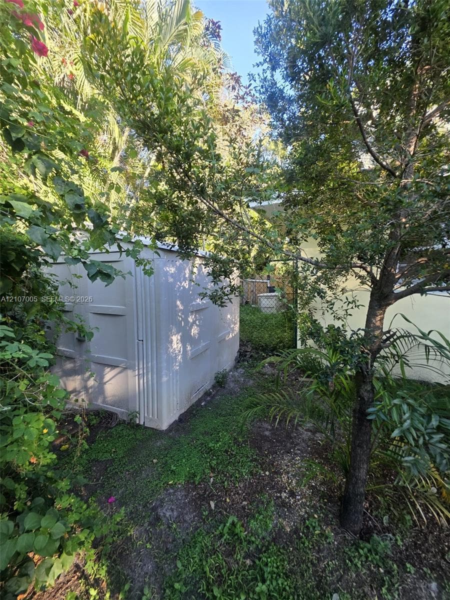 Exterior storage structure featuring a neutral-toned composite exterior, set within a landscaped perimeter of mature trees and established greenery