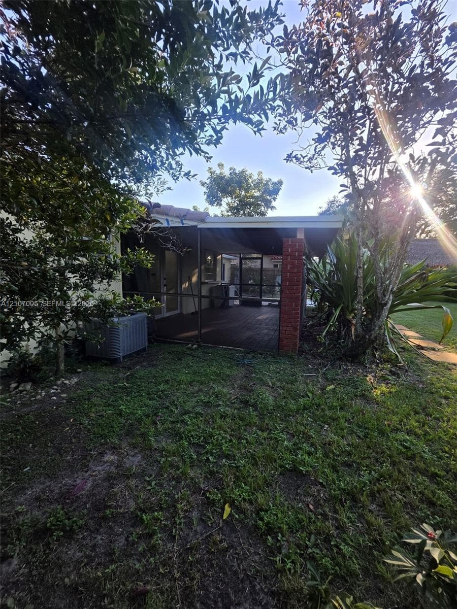 Screened rear patio featuring a brick support column and wood-finish decking, surrounded by mature landscaping