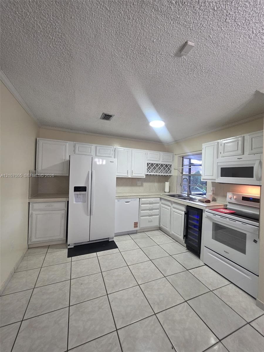 Kitchen featuring white cabinetry, integrated wine storage, tiled flooring, and a suite of white appliances