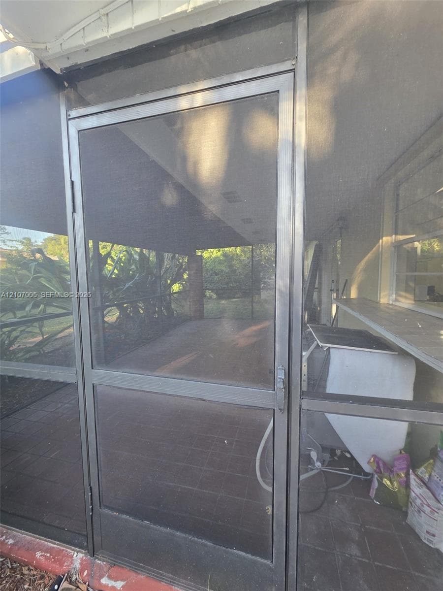 Screened enclosure featuring metal-framed door, tile flooring, and a pass-through service shelf