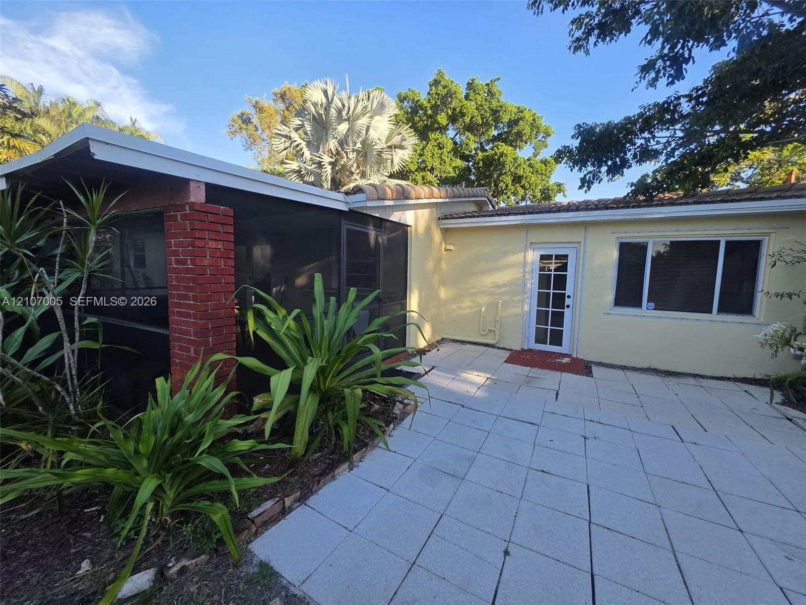 Exterior patio featuring large-format concrete pavers, a screened-in porch with exposed brick column, and a glass-paneled entry door