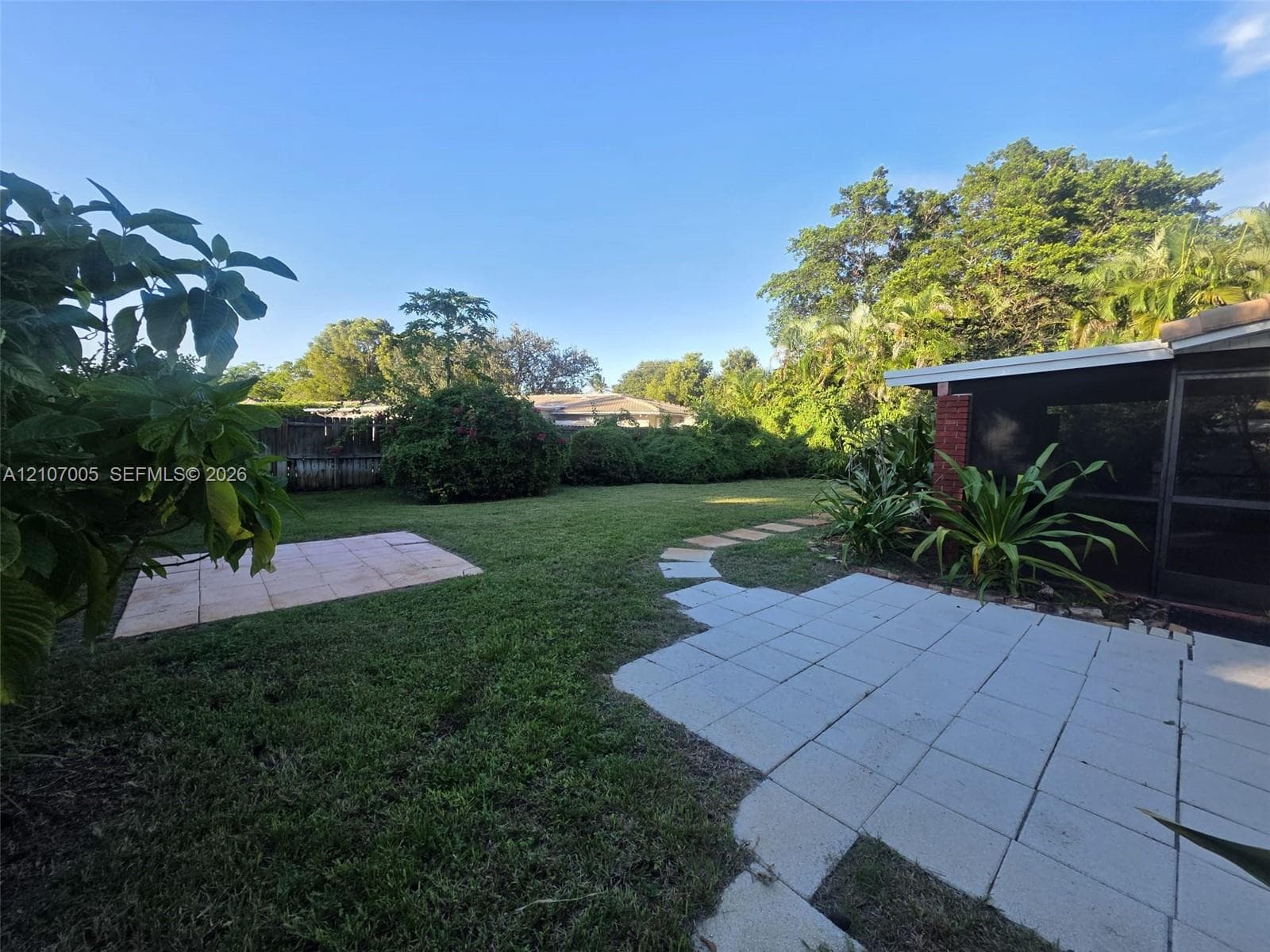 Private backyard featuring a screened enclosure, concrete patio, stepping stone pathway, and mature perimeter landscaping