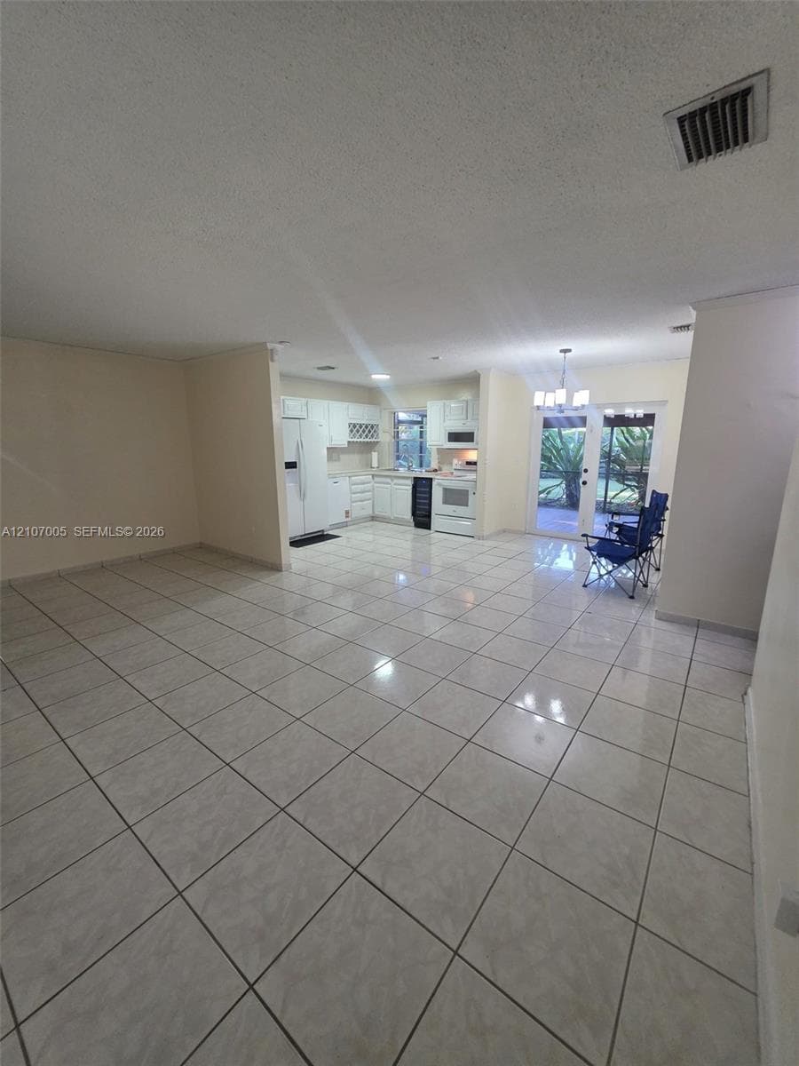 Open-concept interior featuring large-format tile flooring, white cabinetry, integrated wine storage, and glass-paned double doors