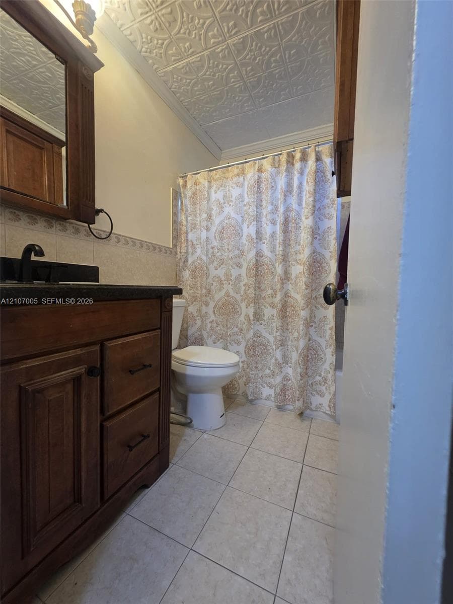 Bathroom featuring a decorative tin-style ceiling, dark wood vanity with a stone countertop, ceramic tile flooring, and patterned wall tile border