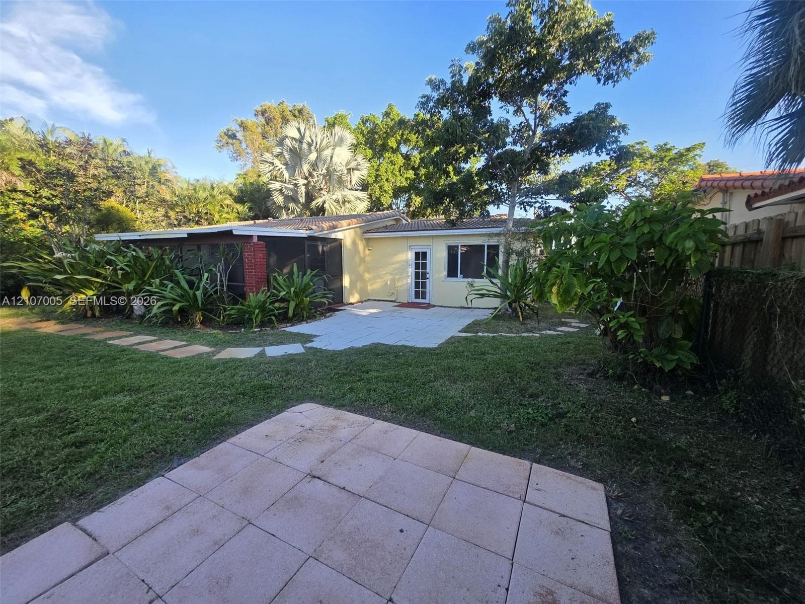 Rear exterior featuring a covered screened-in porch, paved patio areas, and extensive mature landscaping