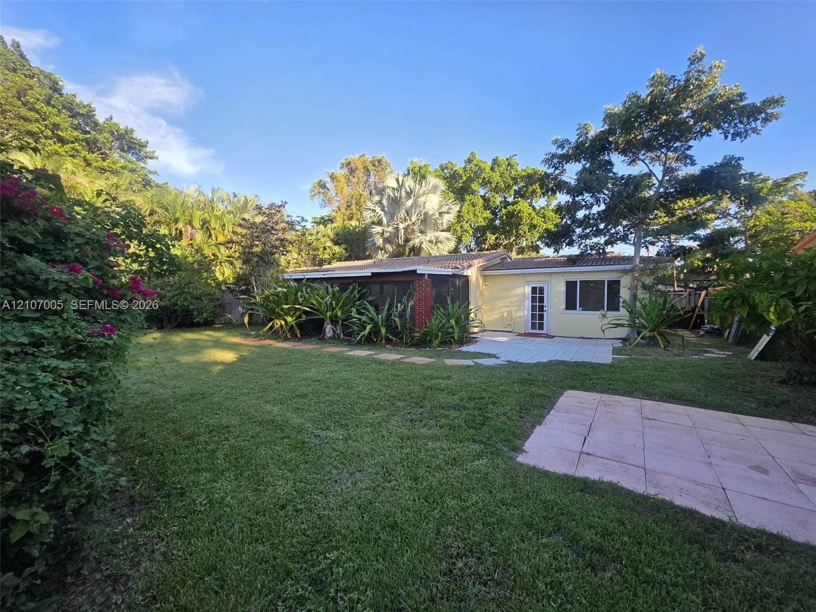 Expansive backyard featuring a lush lawn, paved stone patio, screened-in porch, mature landscaping, and privacy-providing trees