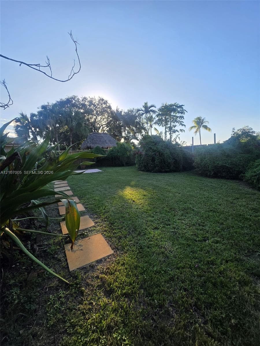 Expansive lawn with stone paver walkway, mature landscaping, and a detached thatched-roof structure