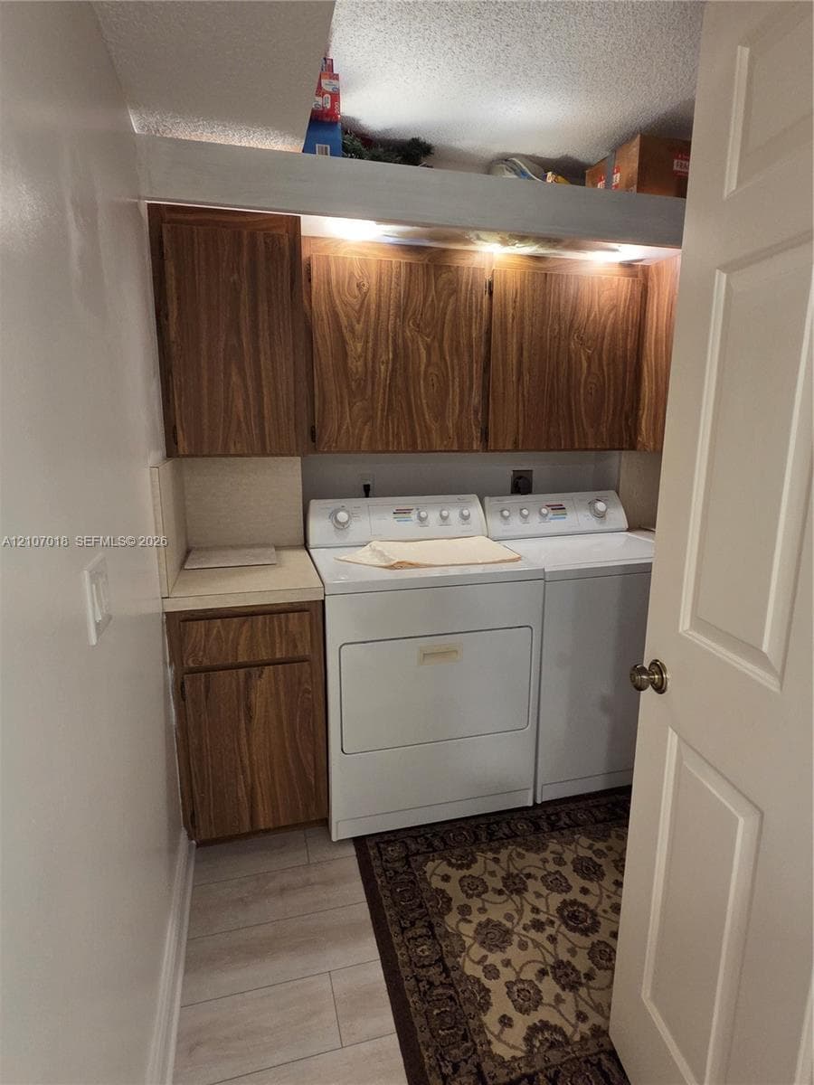 Laundry area featuring wood-finish cabinetry, neutral solid-surface countertop, and light-tone plank flooring