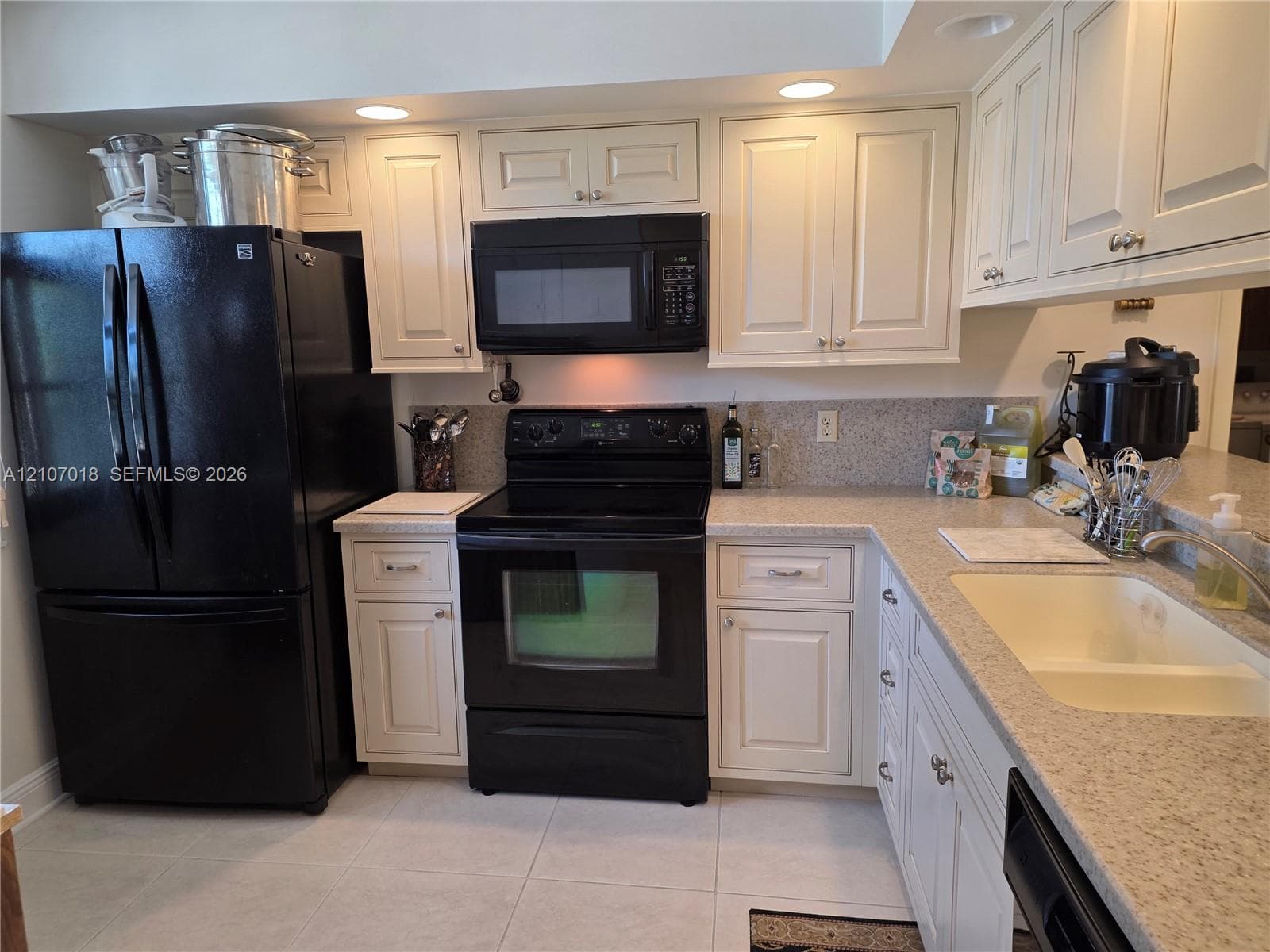 Kitchen featuring off-white cabinetry, black appliances, solid surface countertops, a dual-basin sink, and recessed lighting