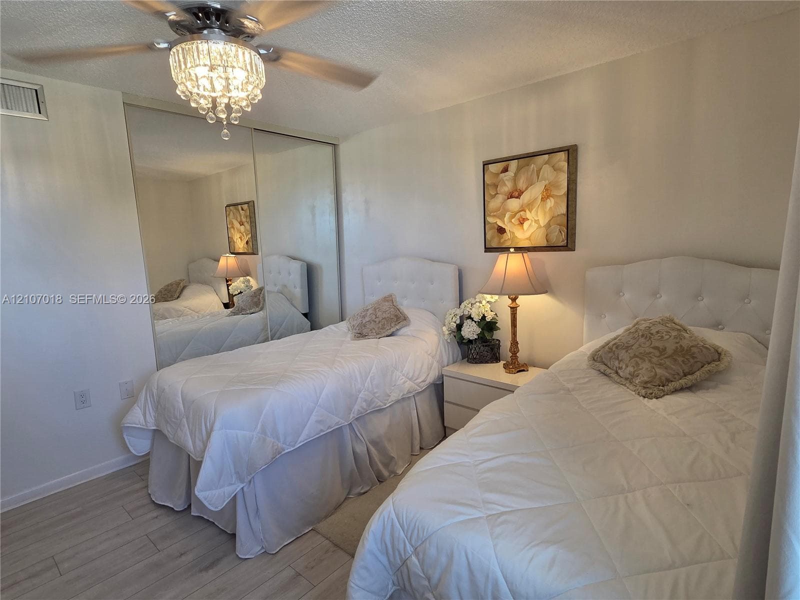 Wood-finish flooring, full-wall mirrored sliding closet doors, and a crystal-accented ceiling fan with light fixture