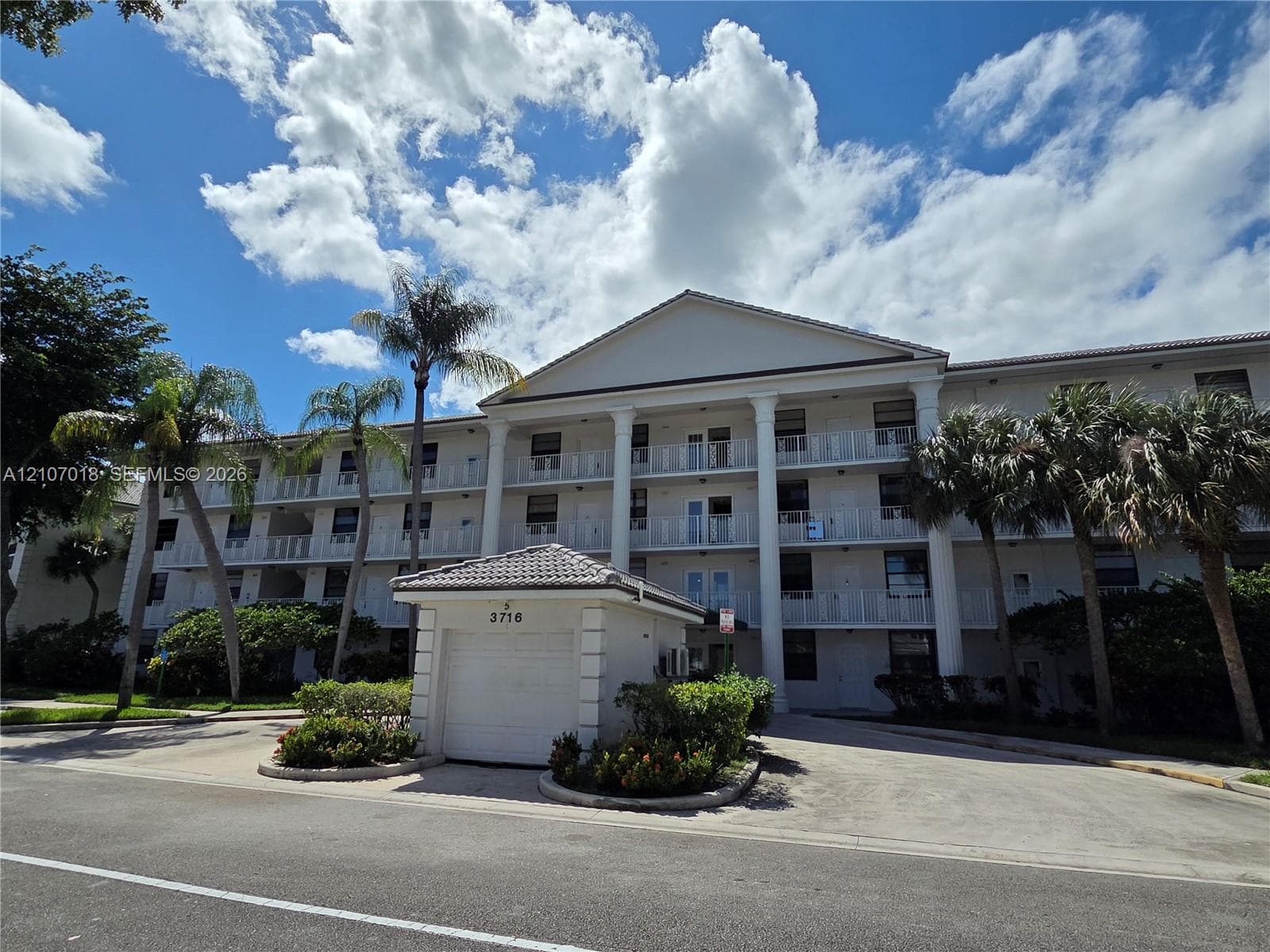 Multi-story building exterior featuring a classic pediment, full-height white columns, multi-level railed balconies, and a detached garage structure