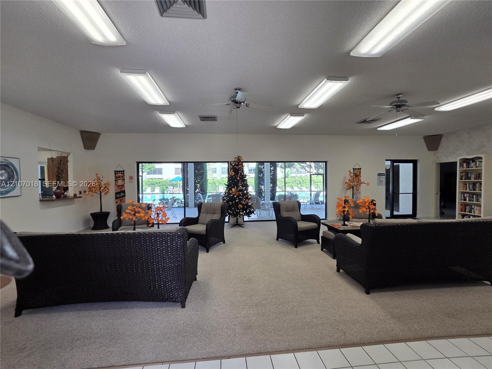 Common area featuring wall-to-wall carpeting, multiple ceiling-mounted fluorescent light fixtures, ceiling fans, built-in shelving, and floor-to-ceiling windows