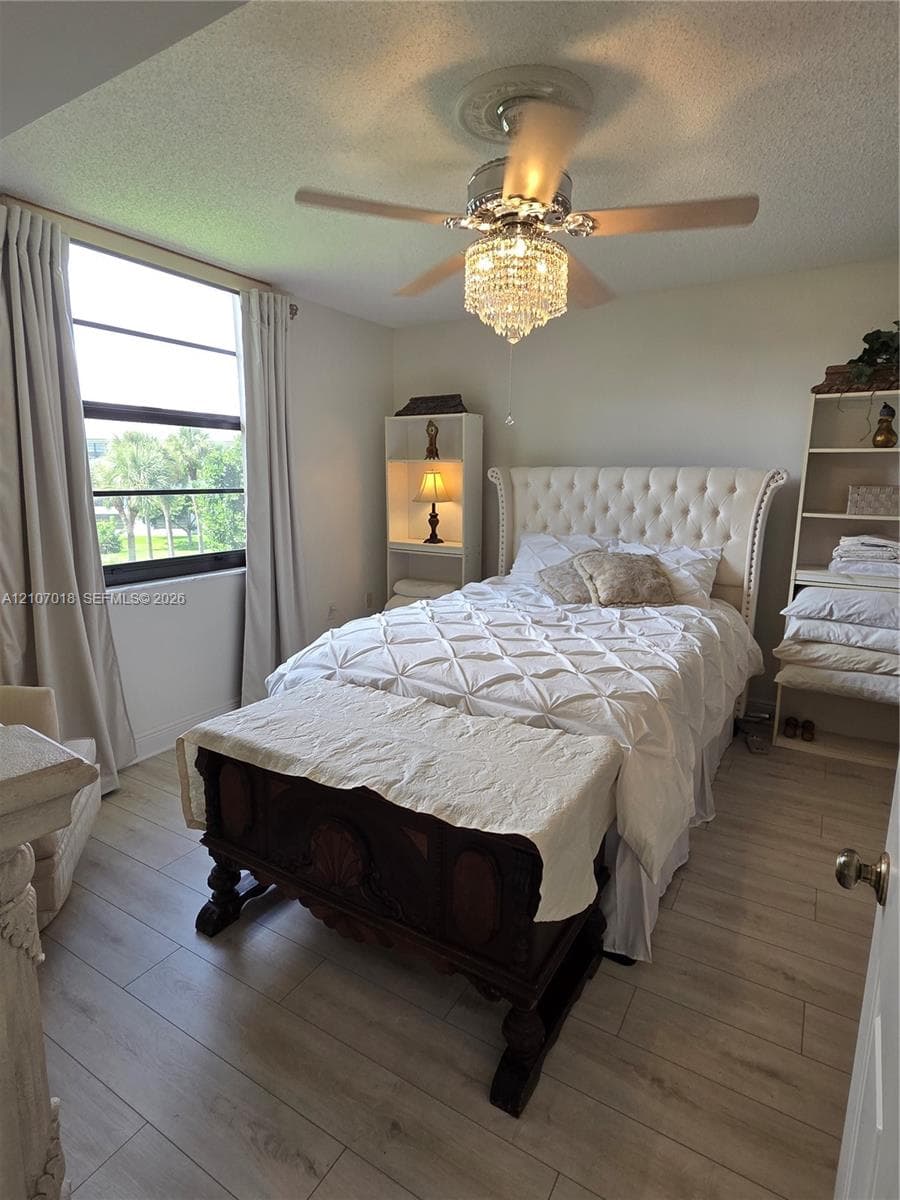 Wood-finish flooring, large-format window with dark trim, and a ceiling-mounted crystal chandelier fan