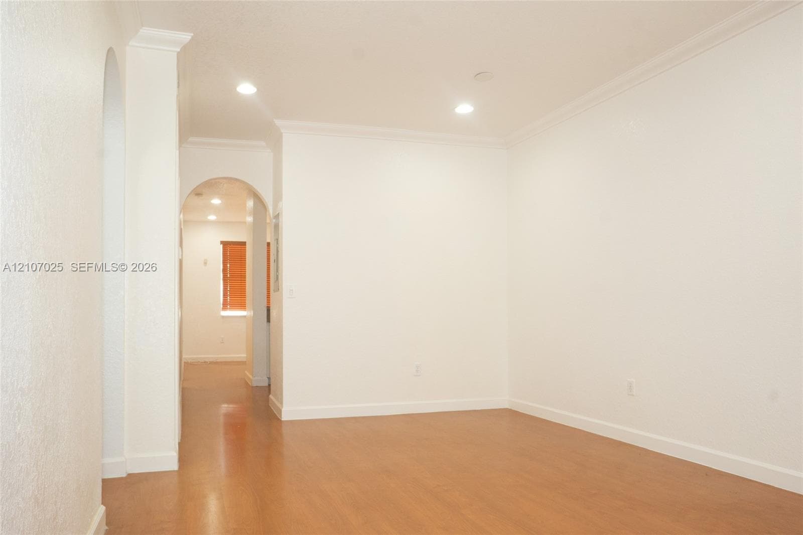 Interior space featuring wood-finish flooring, recessed lighting, crown molding, and an arched architectural opening