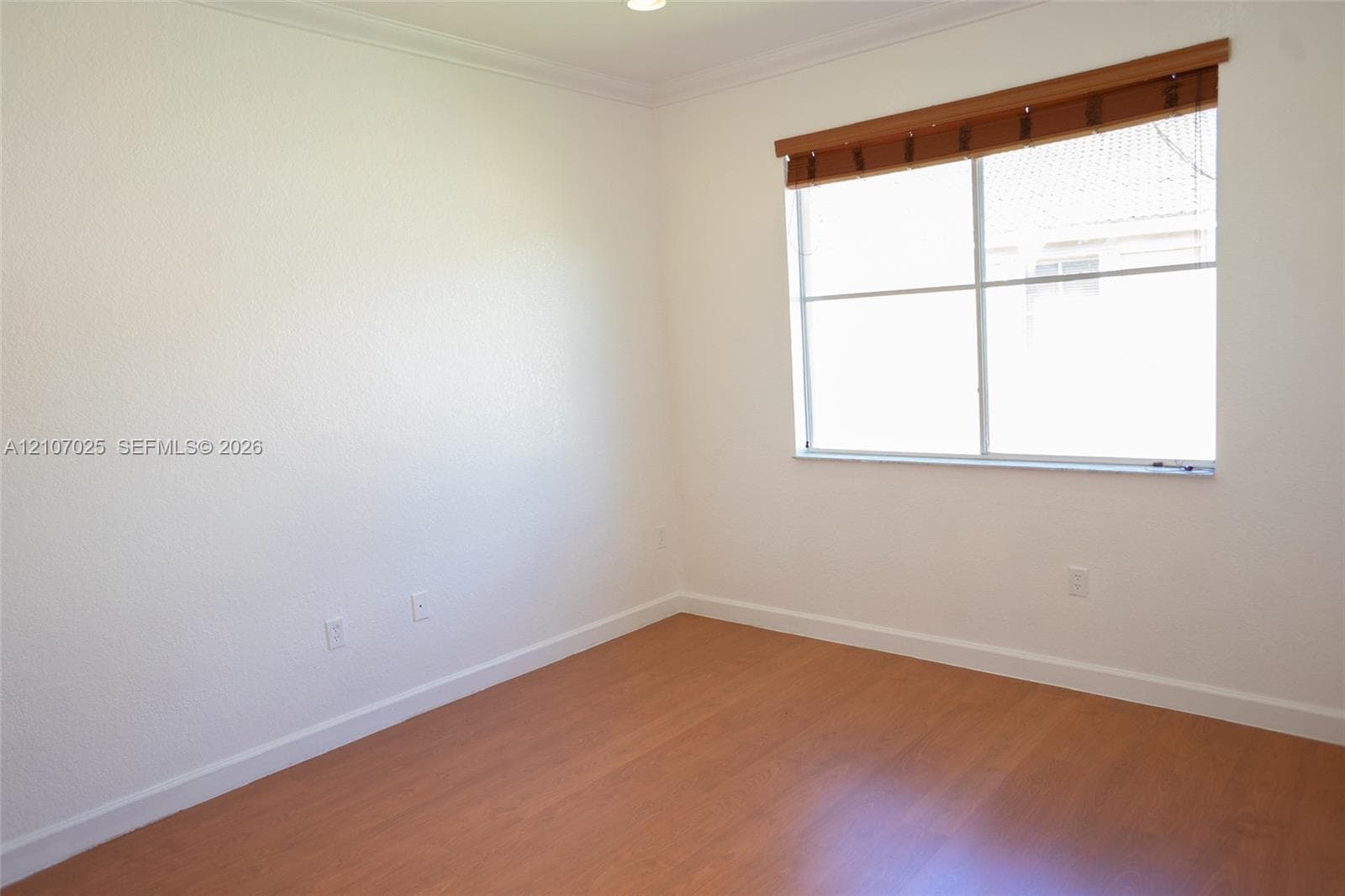 Neutral-toned room featuring wood-finish flooring, textured walls, and a large window equipped with an integrated wood-slat blind