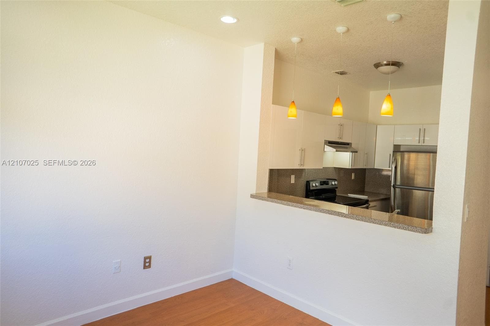 Kitchen featuring white flat-panel cabinetry, stainless steel appliances, a stone-surfaced breakfast bar, and recessed lighting with pendant fixtures over the counter, complemented by wood-finish flooring