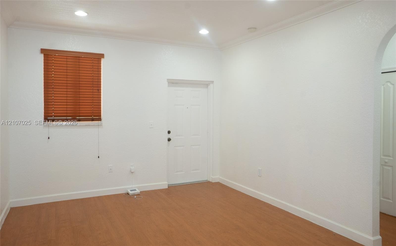 Interior room featuring wood-finish flooring, recessed lighting, crown molding, an arched entryway, and a window with horizontal blinds