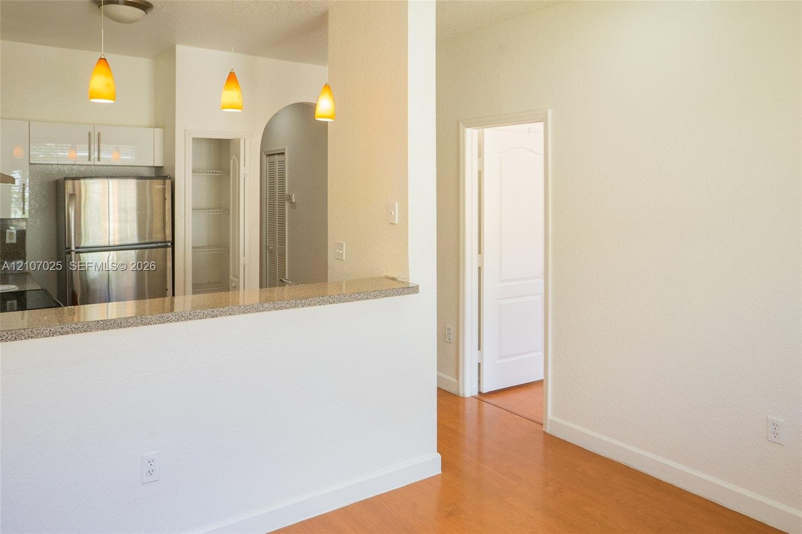 Kitchen featuring a stone-look countertop, white flat-panel cabinetry, stainless steel refrigerator, arched entryway to a built-in pantry, and wood-finish flooring