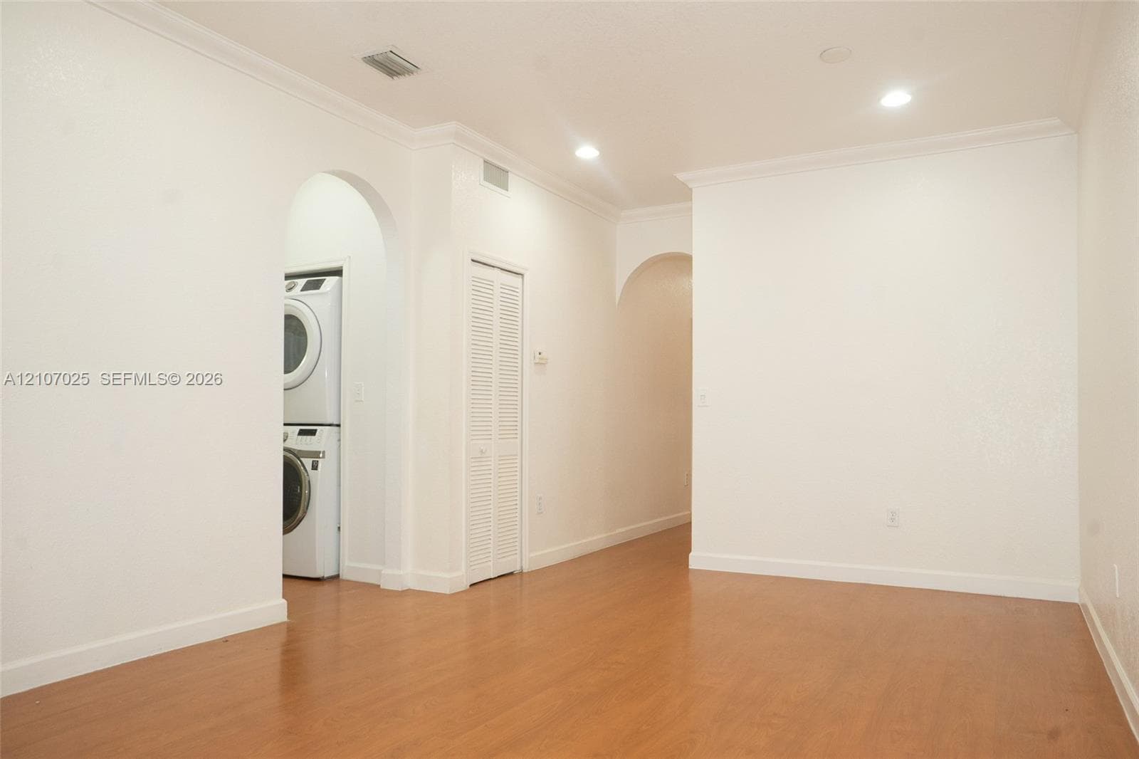 Interior space featuring wood-finish flooring, recessed lighting, crown molding, arched entryways, and a dedicated laundry area with stacked appliances