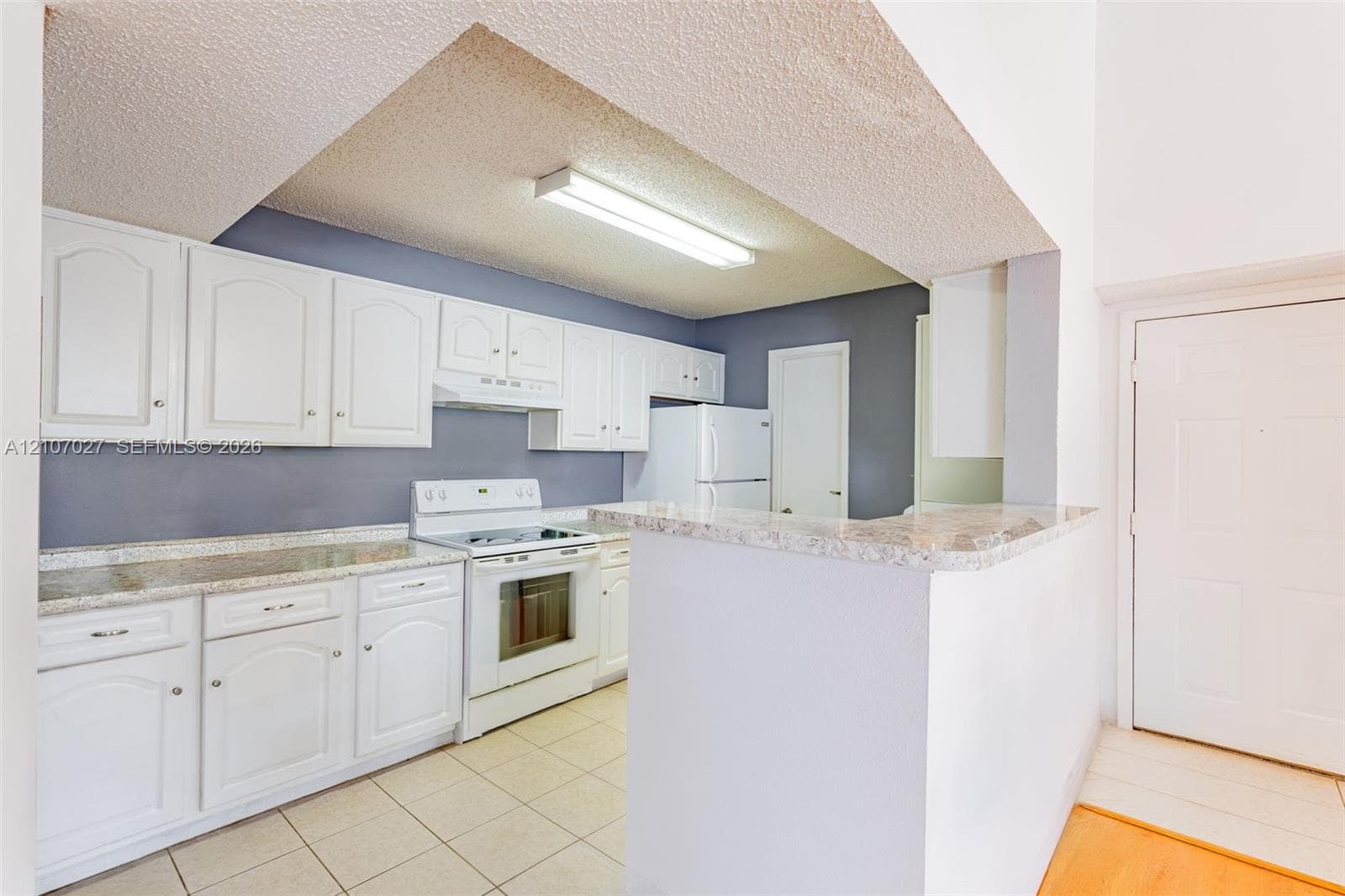 Kitchen featuring white shaker-style cabinetry, solid-surface countertops, tile flooring, and built-in appliances