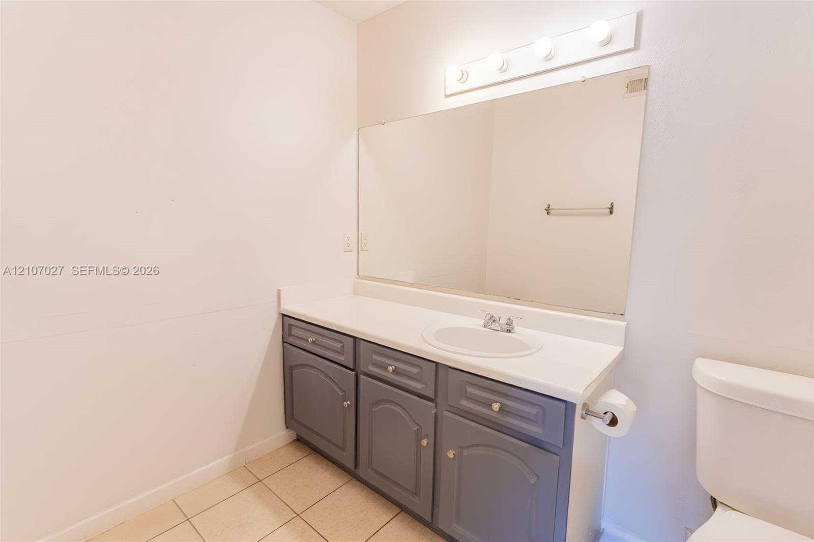 Vanity featuring a solid-surface countertop, integrated basin with a chrome faucet, gray cabinetry, wall-mounted mirror, and a multi-light fixture