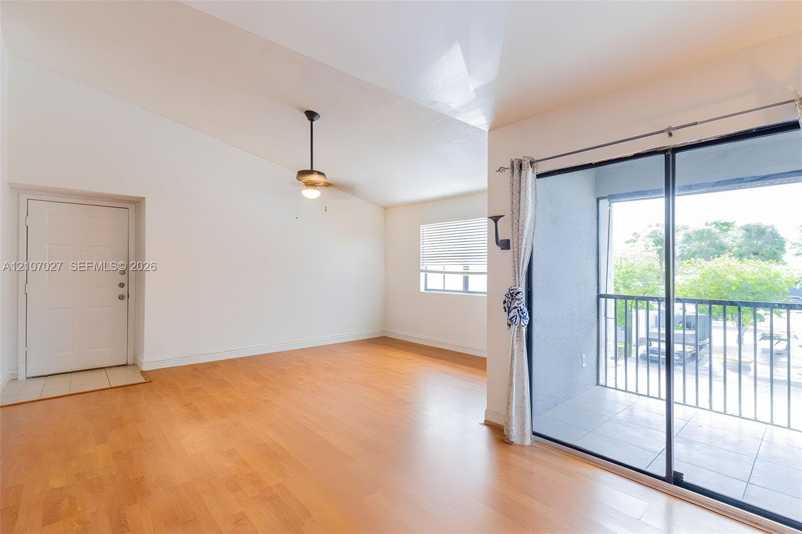Vaulted ceilings, wood-finish flooring, ceiling fan with integrated lighting, and sliding glass doors with direct access to a private balcony