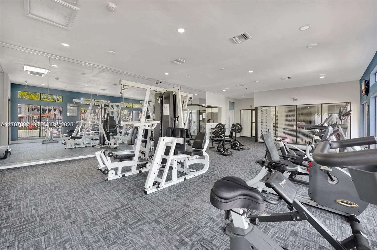 Fitness center featuring wall-to-wall mirrors, recessed lighting, and patterned industrial-grade carpeting