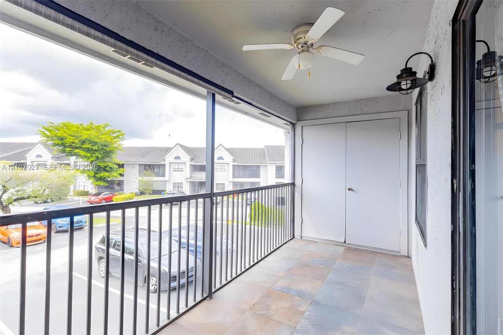 Covered balcony featuring large-format stone-style tile flooring, black metal railing, ceiling fan, and built-in storage closet