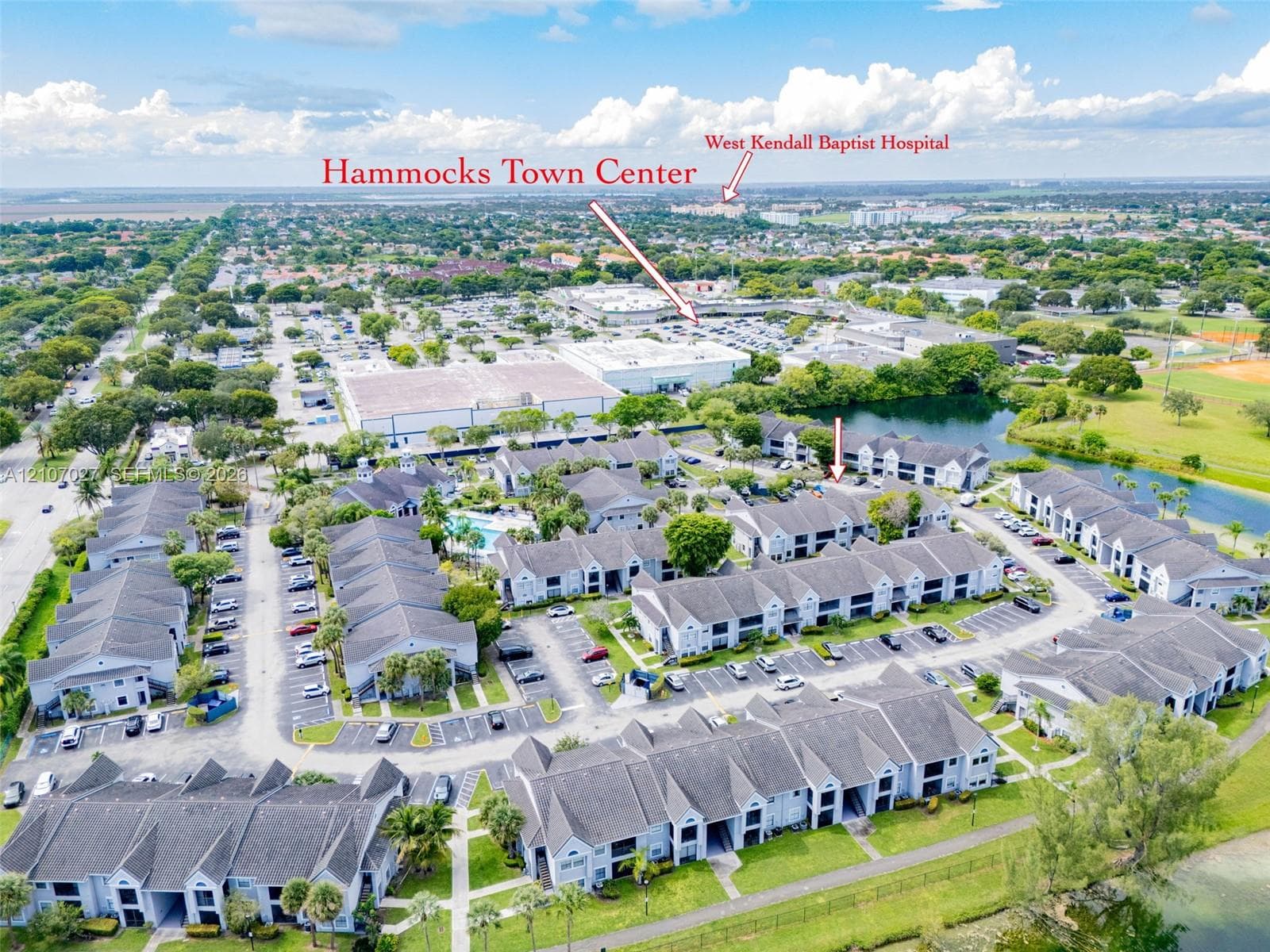 Aerial perspective of a multi-building residential community featuring shingle-style roofing, paved surface parking, mature landscaping, and an onsite swimming pool