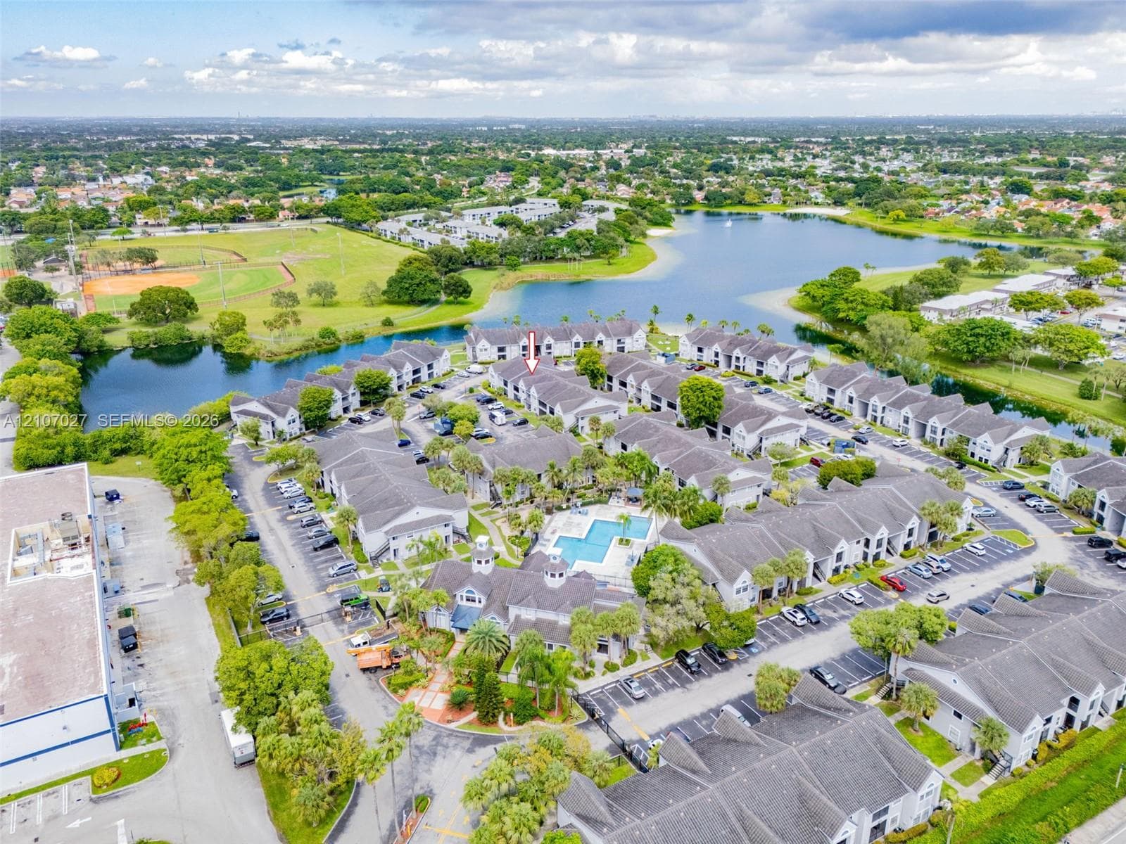 Aerial perspective featuring multi-building residential architecture with shingled rooflines, a central swimming pool, and proximity to expansive natural water features and landscaped grounds
