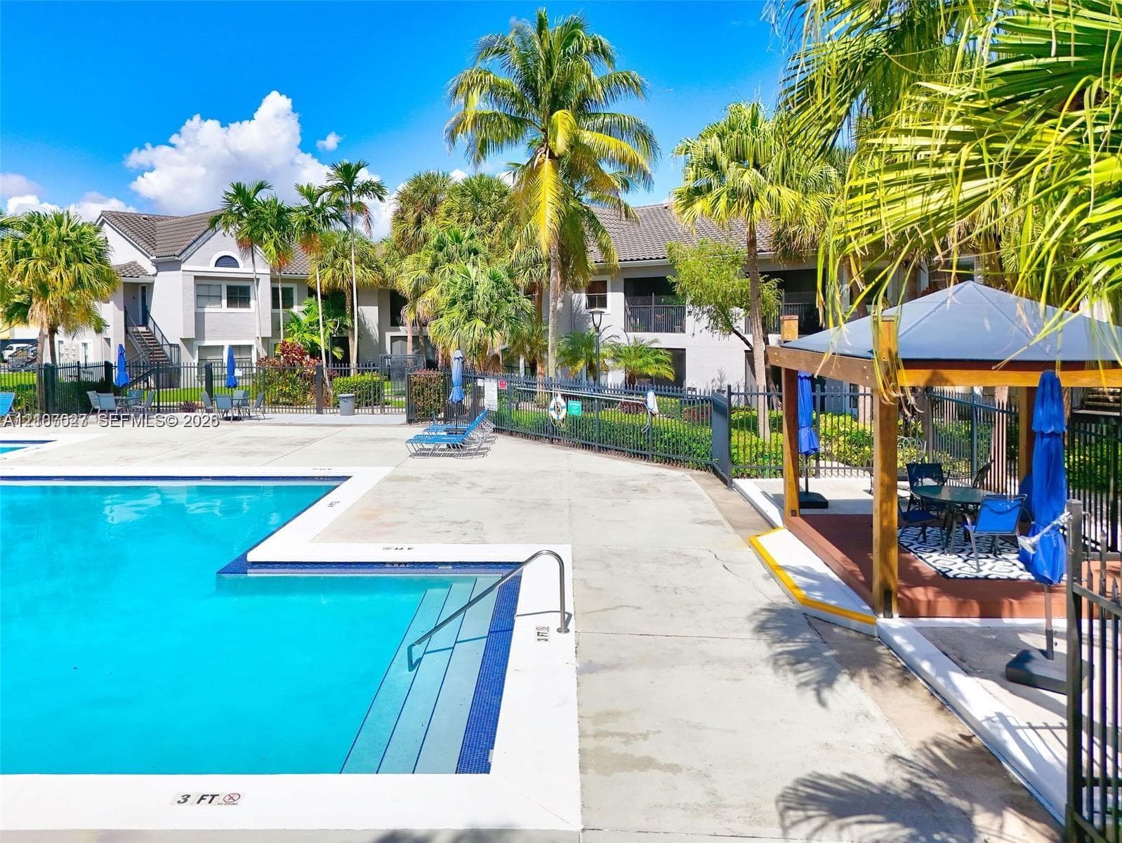 Swimming pool with concrete decking, tiered entry steps, metal safety railing, and a permanent wooden gazebo structure surrounded by landscaping