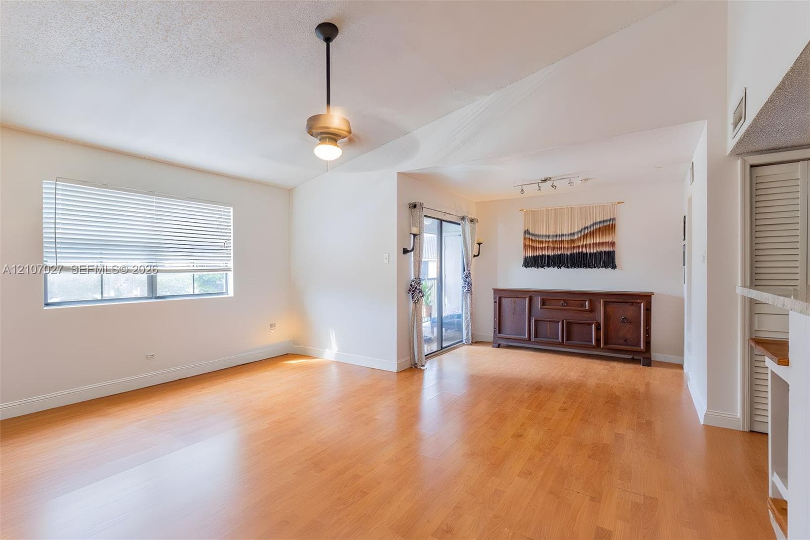 Living area featuring vaulted ceilings, wood-finish flooring, sliding glass patio doors, and a metal downrod pendant light fixture