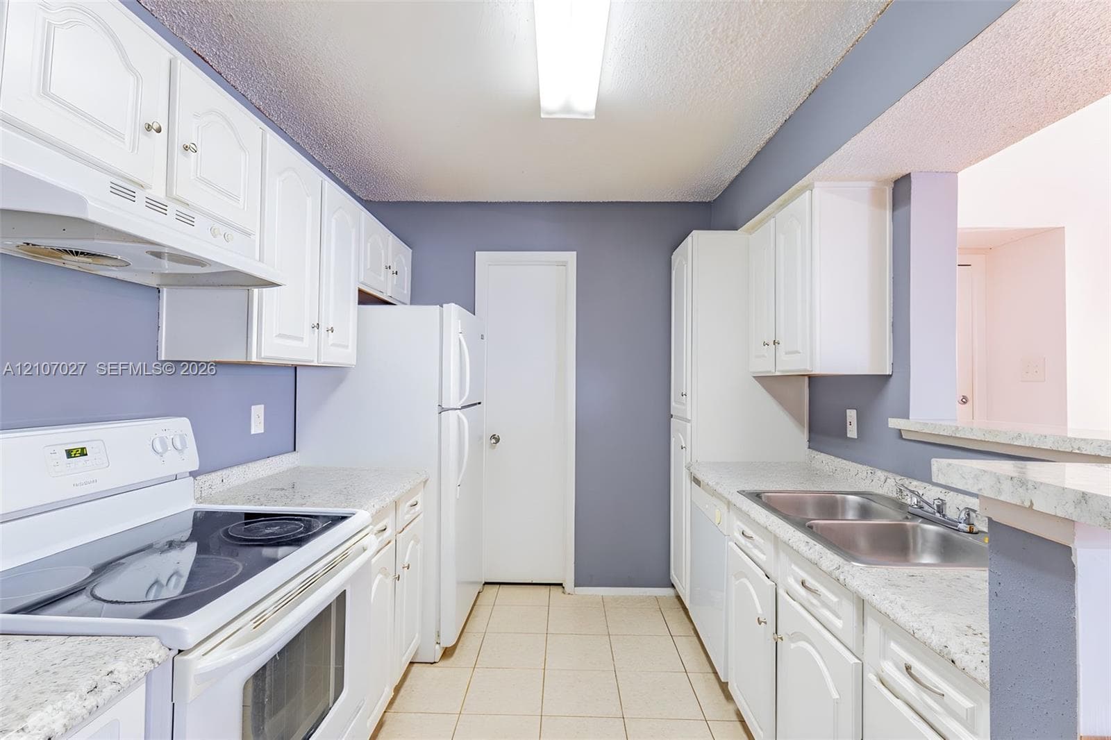 Kitchen featuring white cabinetry, light-toned stone-finish countertops, stainless steel dual-basin sink, and tile flooring