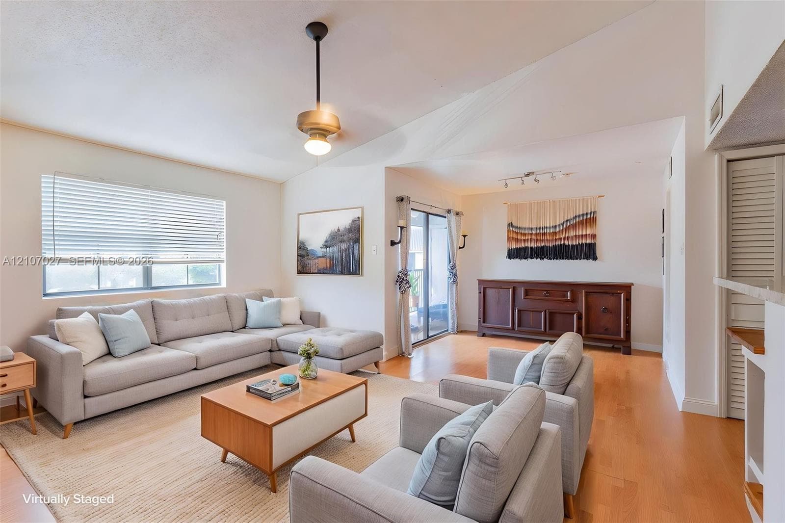 Vaulted ceilings, wood-finish flooring, sliding glass door access to exterior, and a central drop-pendant light fixture