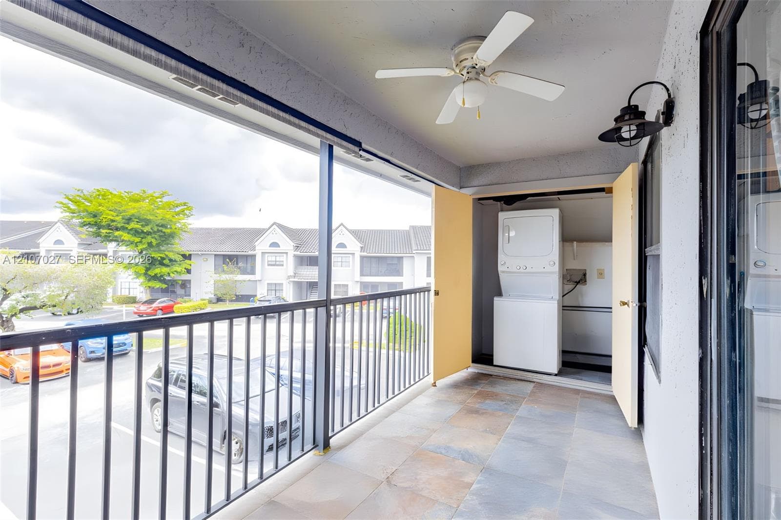 Covered balcony featuring tile flooring, a ceiling fan, black metal railing, and a built-in laundry closet with a stacked washer and dryer