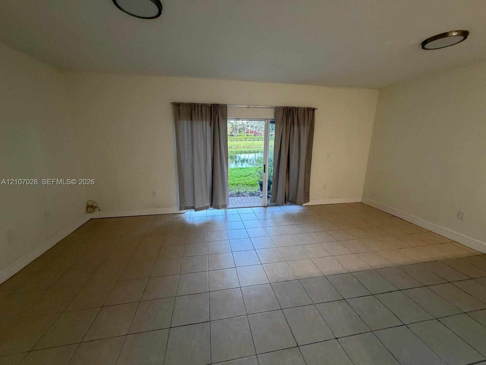 Spacious room featuring neutral ceramic tile flooring, sliding glass doors, and flush-mount ceiling lighting