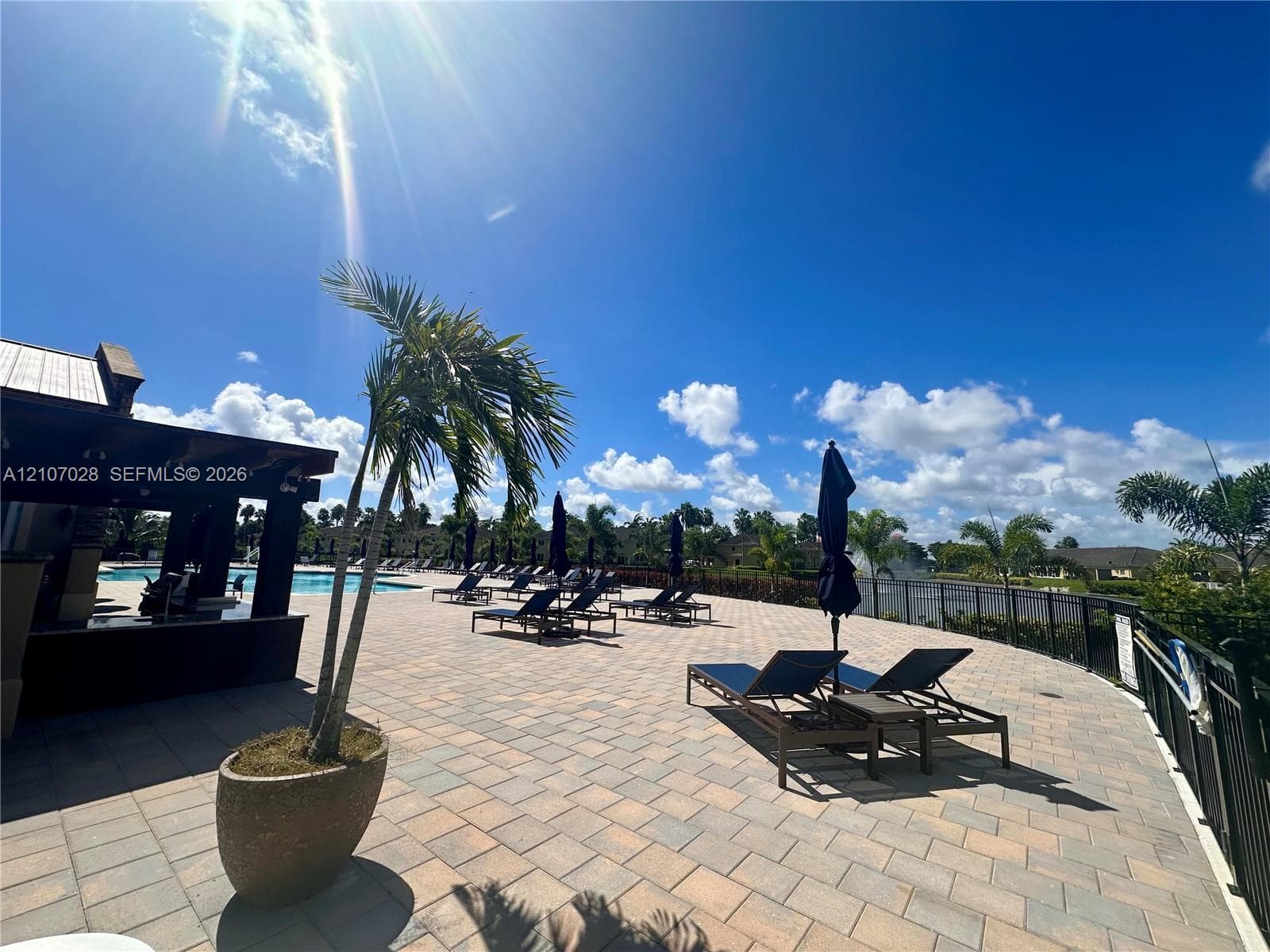 Outdoor patio featuring stone paver flooring, a covered bar structure, and perimeter metal fencing