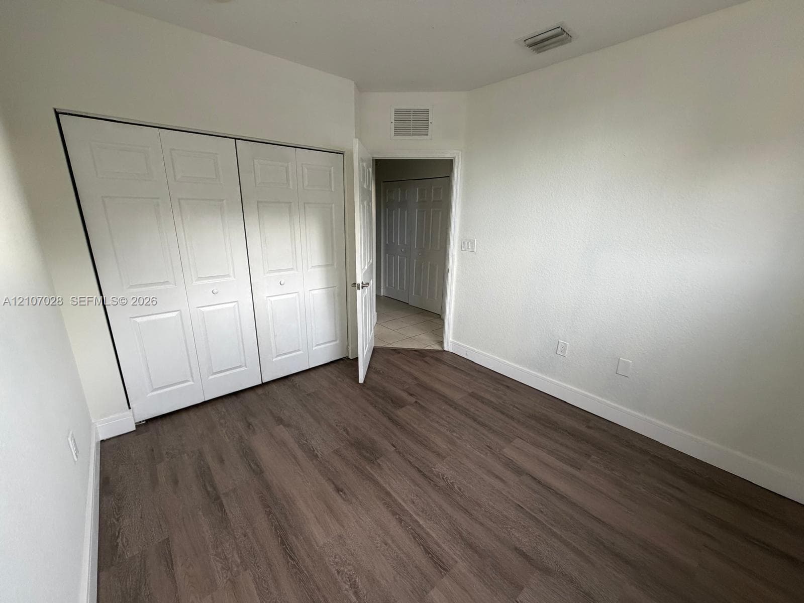 Room featuring wood-finish flooring, white walls, and a multi-panel interior closet door