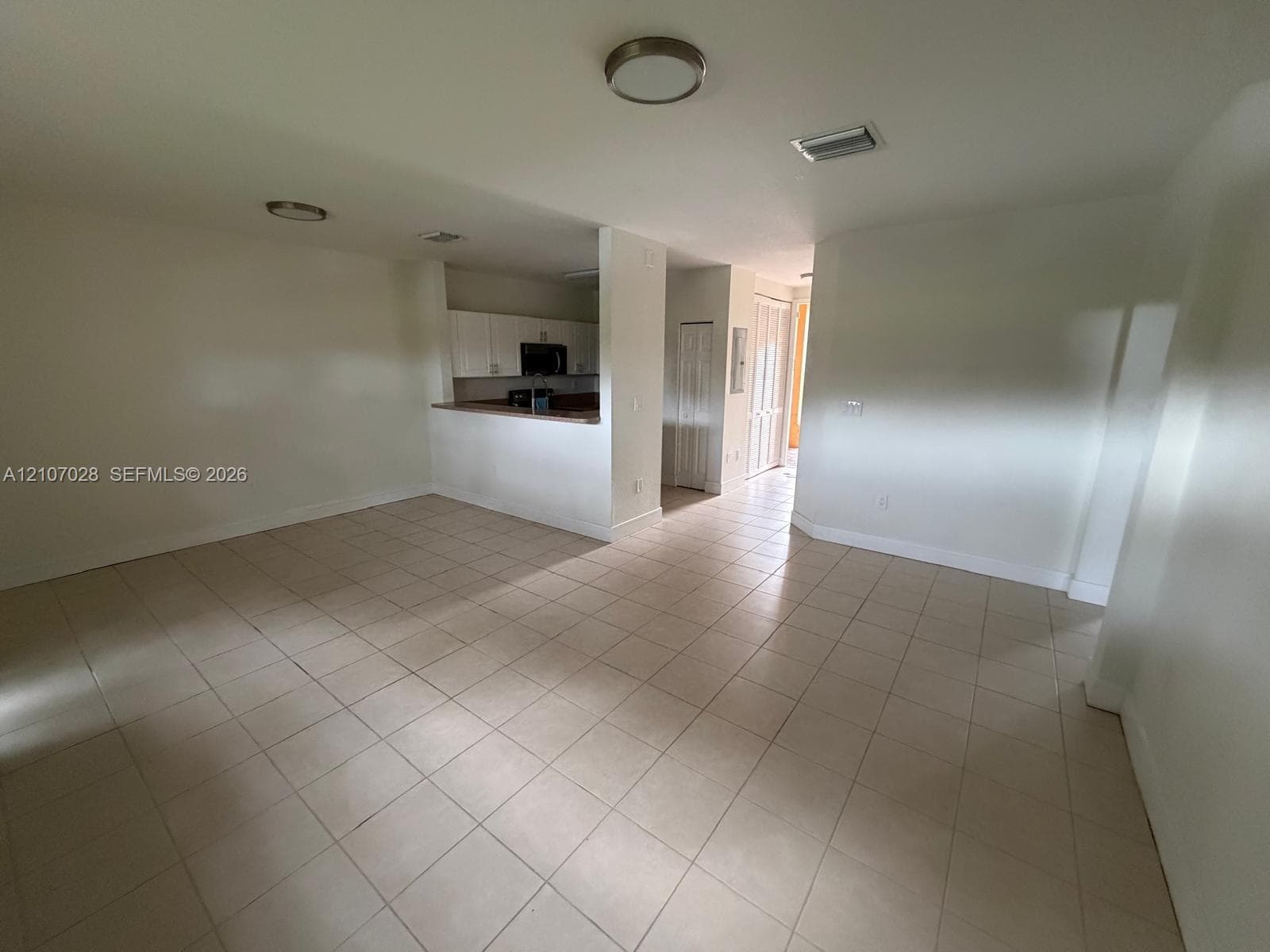 Open-concept interior featuring neutral tile flooring, recessed ceiling lighting, a pass-through kitchen counter, and crisp white cabinetry