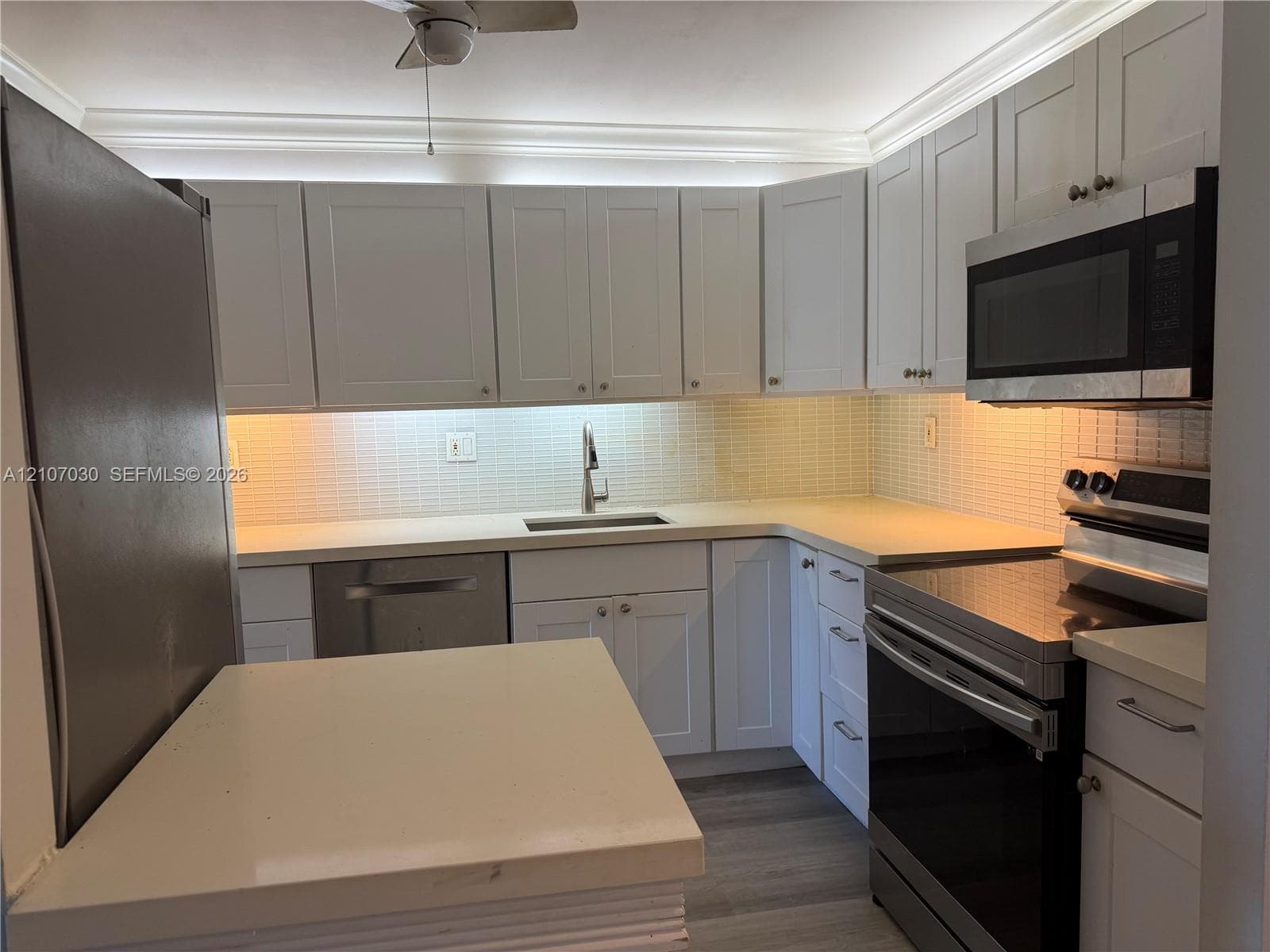 Kitchen featuring white shaker-style cabinetry, solid-surface countertops, a tiled backsplash, wood-finish flooring, and stainless steel appliances