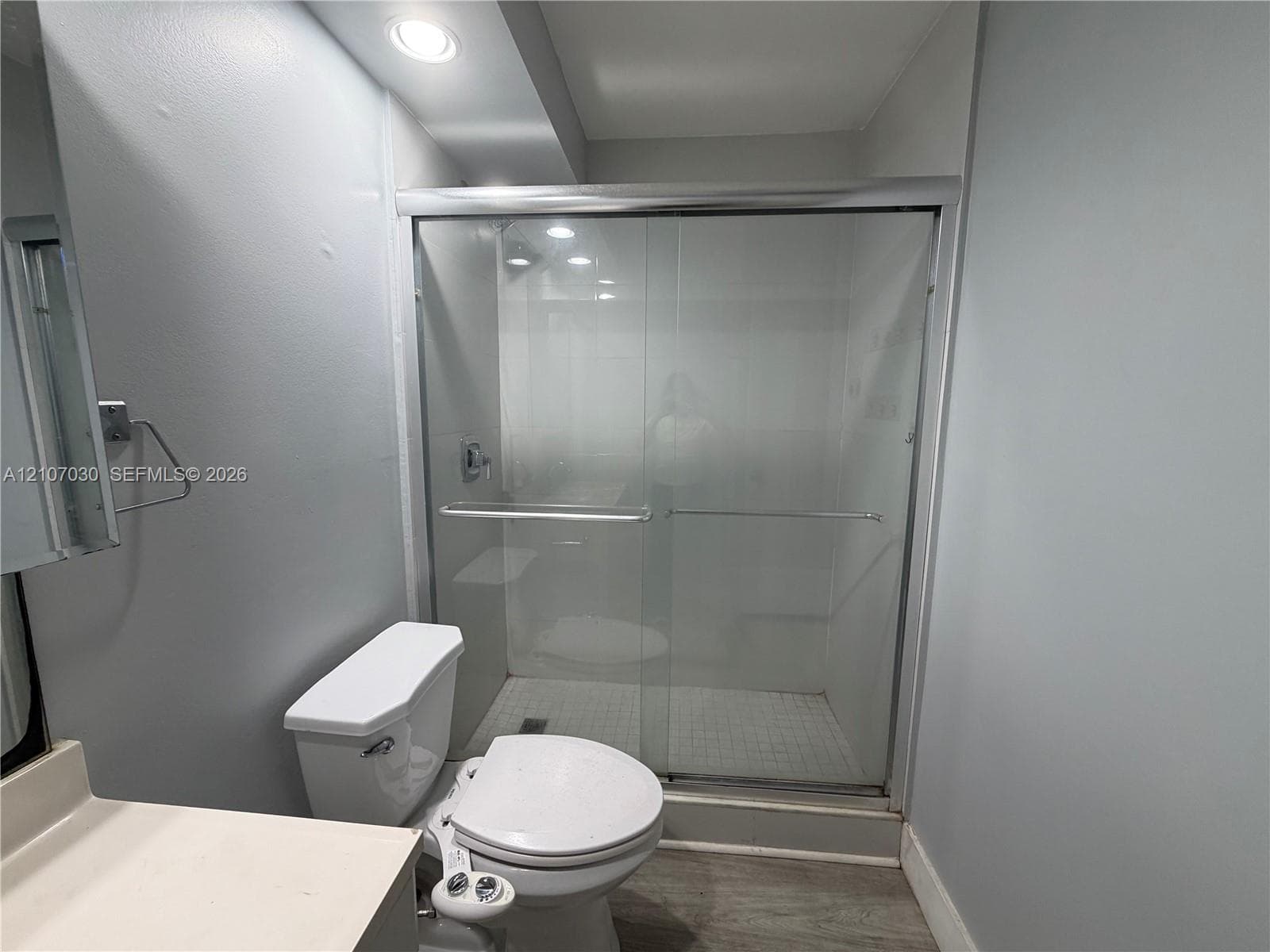 Shower enclosure with sliding glass doors, tiled floor, recessed lighting, and white toilet