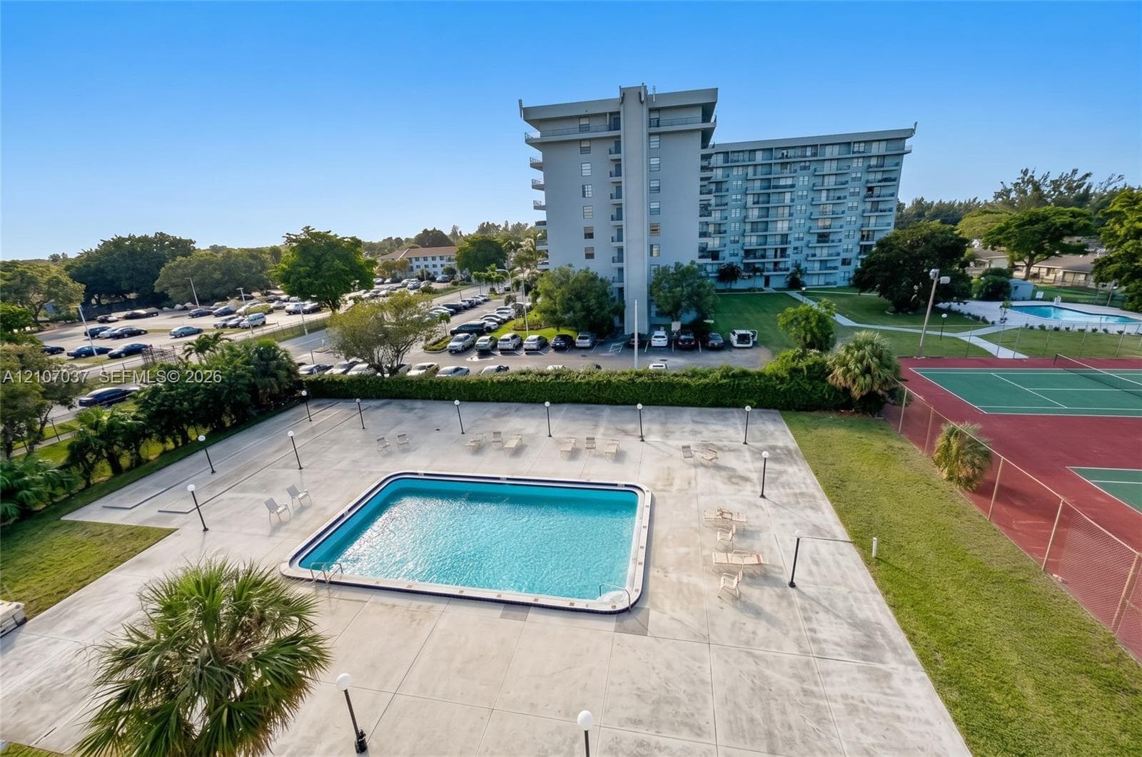 Outdoor area featuring a swimming pool, concrete deck, fenced tennis courts, and mature landscaping