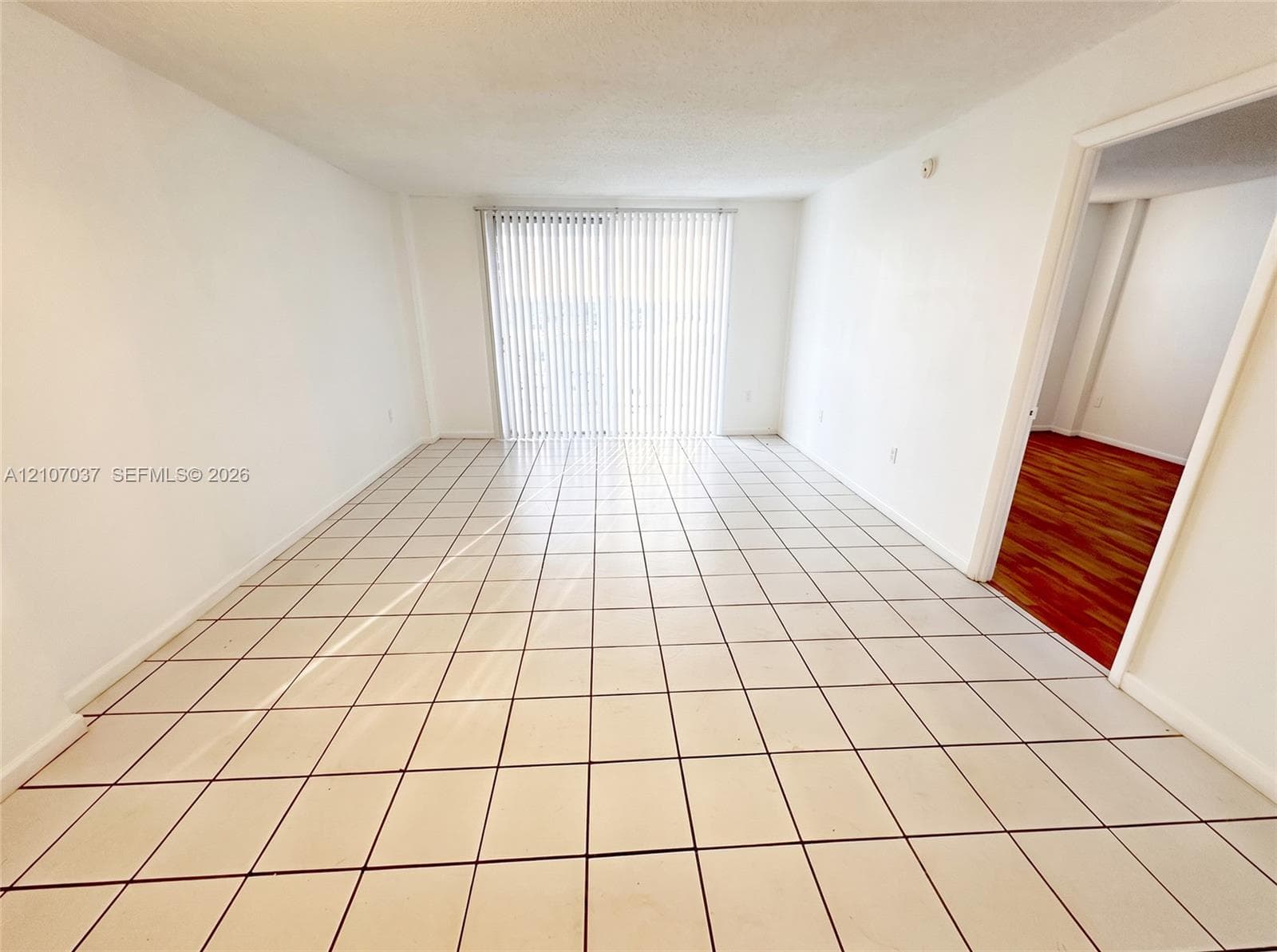 Interior space featuring white tile flooring, neutral walls, and a glass sliding door with vertical blinds