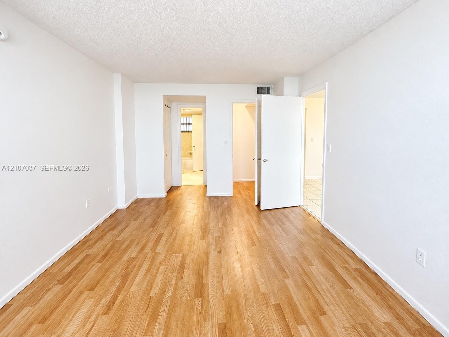 Interior space featuring wood-finish flooring, white walls, and multiple closet entries