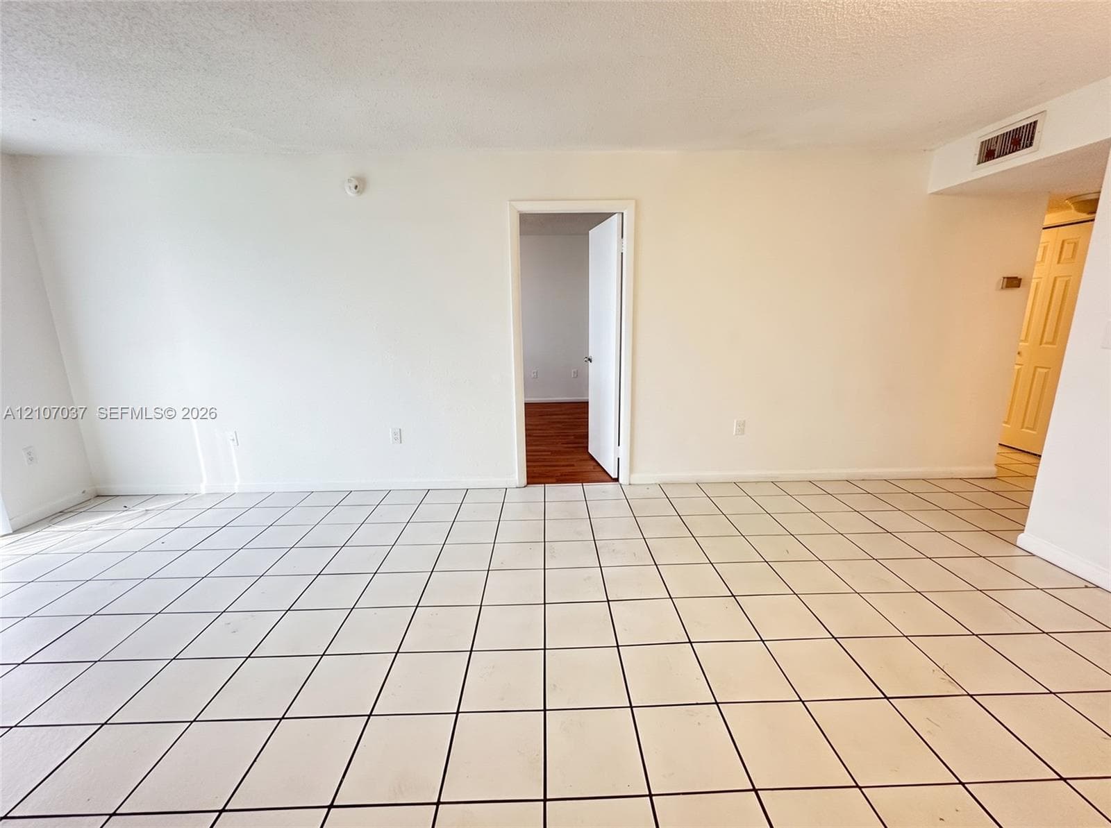 Interior space featuring light-colored ceramic tile flooring, smooth white wall finishes, and a wood-finish floor in the secondary room